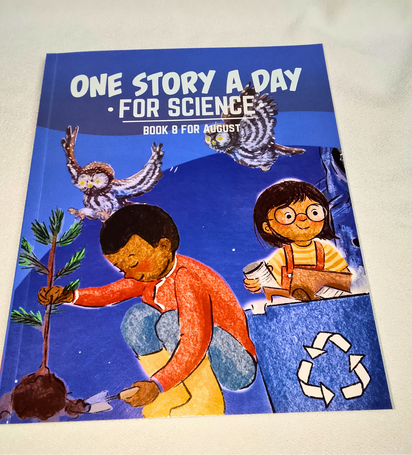 Book titled 'One Story A Day For Science' with illustrations of children and a tree on a blue background.