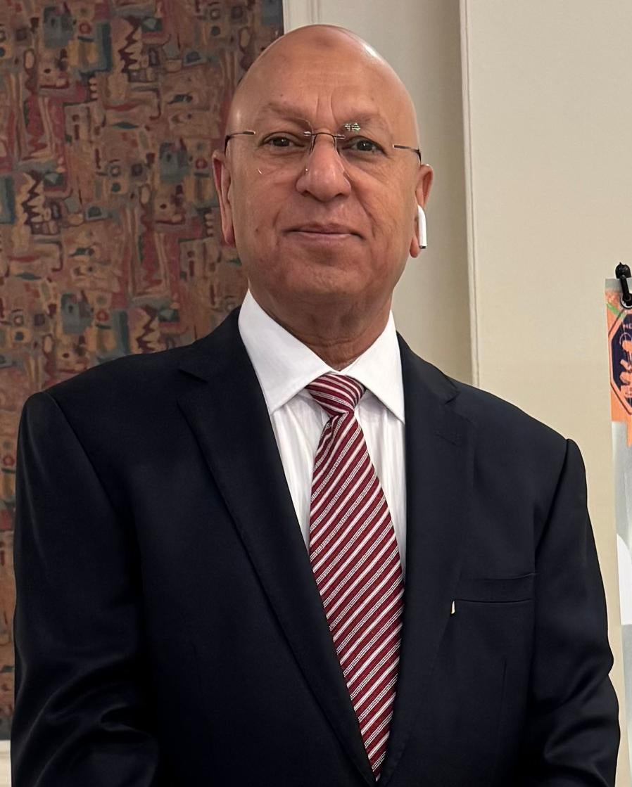 Man in a suit and tie standing in an office setting with a colorful wall and poster in the background.