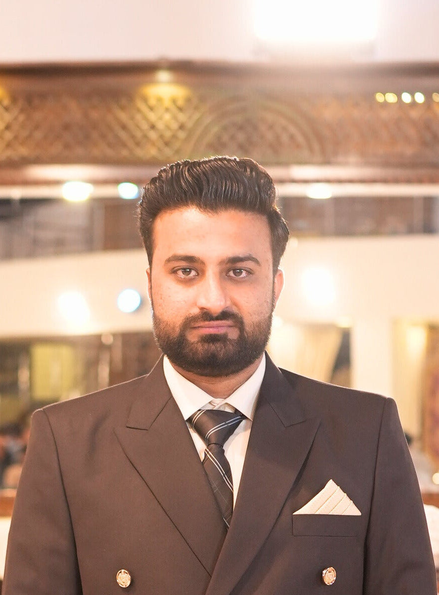 Man in a suit standing in a decorated indoor setting with people in the background.