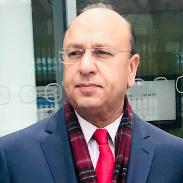 Man in a blue suit with a red tie and plaid scarf standing outdoors.